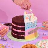 Design your own Cake being decorated with pastel icing, meringues, and sprinkles by Crumbs & Doilies experts